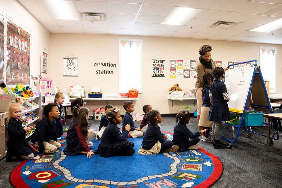 Young students sitting on a colorful rug as their teacher reads