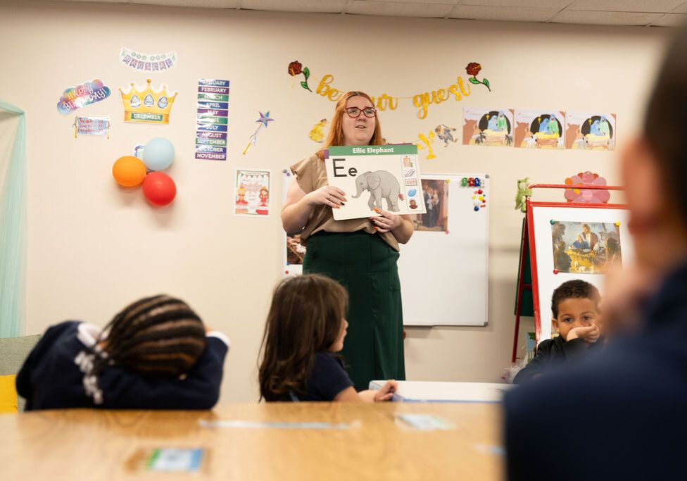 A preschool teacher holding up a letter card for the class